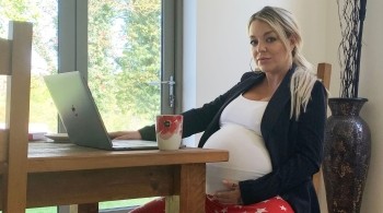 A pregnant Sheridan Smith sits in front of a laptop at a kitchen table 