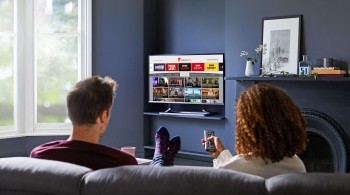 Couple looking at the Explore Freeview Play interface on their TV, about to click onto BBC Sounds